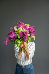 A faceless Caucasian woman holding a bouquet of flowers in her hands on a dark background. Spring concept.