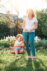 Happy International Children's Day. A young mother having fun with a her happy toddler on a swing....