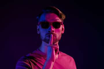 Portrait of attractive mysterious guy showing shh sign keep silence isolated over dark neon violet...
