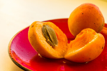 halves of a large fresh apricot on a red saucer, close-up