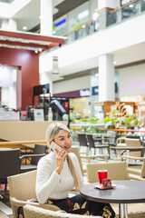 Vertical shot of a blonde Hispanic female talking on the phone in cafe