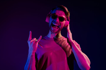 Portrait of attractive cheerful crazy guy listening bass sound showing horn sing fooling isolated over dark neon violet color background