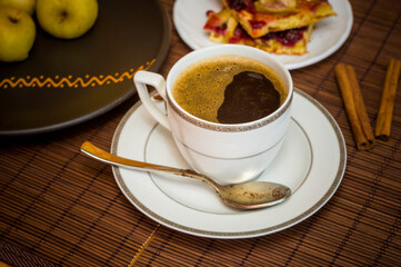 Still life - a hot cup of black coffee, homemade cookies with fruit, baked apples on a bamboo mat