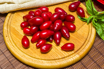 Still life - fresh large dogwood berries, purple plums and a sprig of basil on a wooden board