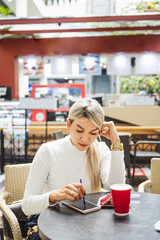 Vertical shot of a blonde Hispanic female using her phone in a cafe