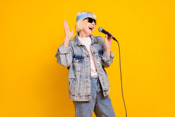 Photo portrait of senior woman wearing sunglass denim outfit singing in microphone on stage isolated vivid yellow color background