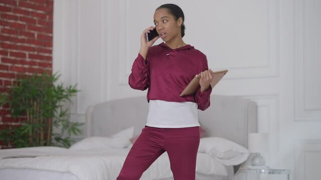 Arrogant self-confident young woman talking on the phone standing in bedroom hanging up and leaving. Portrait of assertive beautiful African American CEO with laptop working from home office