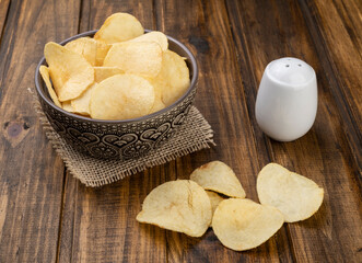 Potato chips in a bowl with salt over wooden table