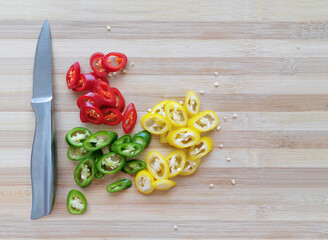 Chopped red, green and yellow chillies with a knife on a bamboo chopping board.  - Powered by Adobe
