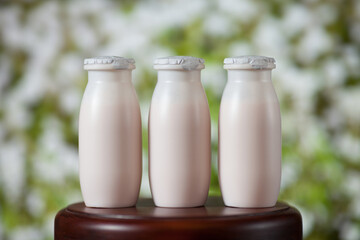 Natural liquid yogurt with probiotics in small plastic bottles on wooden table on background of meadow with flowers.