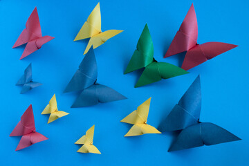multicolored origami paper butterflies of different sizes on a blue paper background