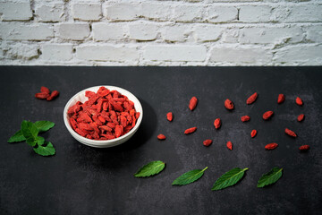 Goji Beeren in einer Schale. Pfefferminzblätter auf dem Untergrund.