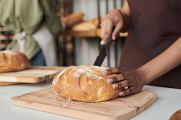 Close-up of woman cutting baked fresh bread in the bakery