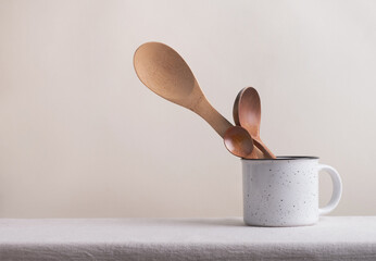 Ceramic mug with wooden spoons on table. Cooking concept, home kitchen utensils, scandinavian style. Minimal composition pastel beige colors. Copy space