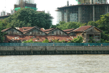 Decrepit stilt housing from Chao Phraya River in Bangkok with modern construction in the background