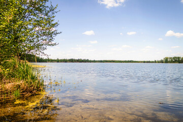 The blue lake reflects the sky and clouds. It s a sunny summer day.