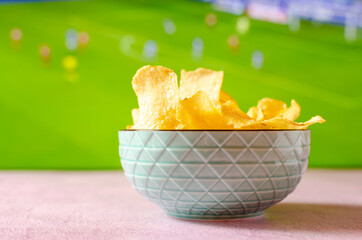 Bowl of potato chips to watch soccer. Snack with out of focus sports background.