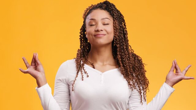 Young positive african american woman making mudra gesture and meditating, smiling and breathing, orange background