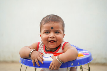 Cheerful Indian origin small boy, Kala tikka applied on his forehead, standing on a baby walker