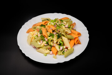 serving of colored penne pasta with tomato sauce, ham and basil