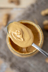 Peanut butter in an open jar and heap of nuts on wood background.