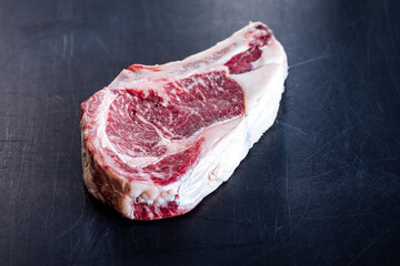Dry aged and raw Rib eye steak isolated on a black cutting board