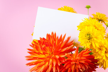 Blank greeting card in bouquet of yellow and red summer flowers on pink background. Holiday invitation, place for text.