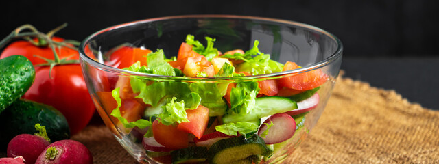 Fresh vegetable salad in a glass bowl on dark background. Vegan organic food, seasonal summer dish.