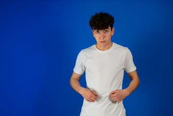 Portrait of attractive young man with curly hair posing on blue studio background