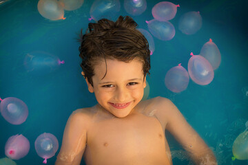 6 Year Old Boy In The Pool With Water Balloons. Summer Concept.