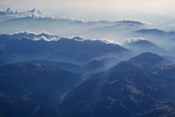 Aerial view of misty mountains and clouds above the mountain peaks, blue tinted