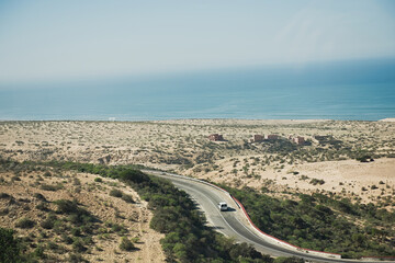 car on a highway that runs along the Ocean from one side and Mountains at Sahara Desert from the other in Morocco,