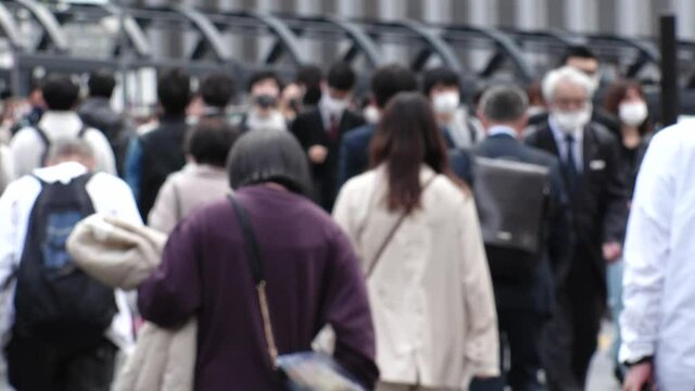 OSAKA, JAPAN - APRIL 2021 : Crowd of people wearing surgical masks to protect from Coronavirus (COVID-19) at the street in busy rush hour. View of commuters after work around Osaka train station.
