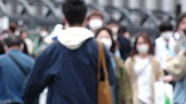 OSAKA, JAPAN - APRIL 2021 : Crowd of people wearing surgical masks to protect from Coronavirus (COVID-19) at the street in busy rush hour. View of commuters after work around Osaka train station.