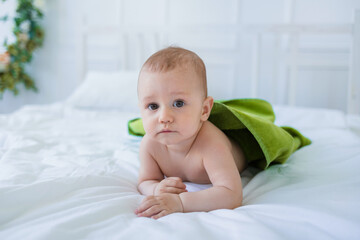 baby boy with a green towel is lying on a cotton blanket on the bed. Summer air treatments