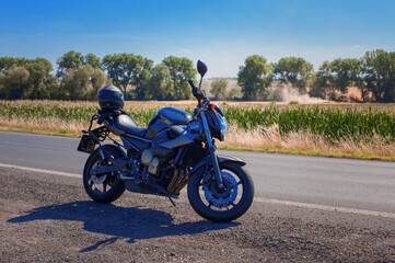 motorcycle on the side of a rural road by covered with sun-filled agricultural fields at the golden hour