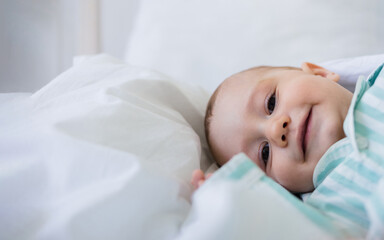 baby boy in striped pajamas lies on a white cotton blanket on the bed. The baby woke up