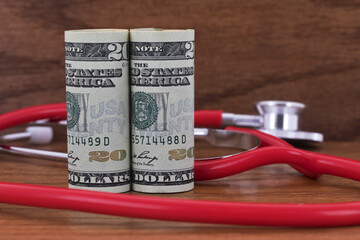 American currency and red stethoscope on wood background reflect need to support medical initiatives