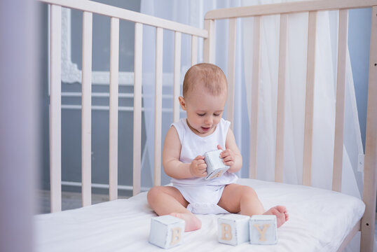 smart little boy in a white bodysuit sits in a child's bed with wooden cubes. Early child development