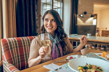 Dark-haired pretty woman sitting at the table in a restaurant and looking contented