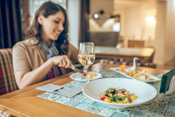Dark-haired pretty woman sitting at the table in a restaurant and looking contented