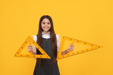cheerful teen girl hold math triangle ruler in school on yellow background, education