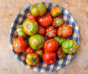 Organic and ecological tomatoes of different sizes, in a rustic deep plate, on a wooden board.