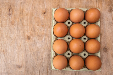 Twelve fresh eggs in a box, on a wooden board.