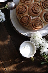 Cinnamon rolls on the table with white lilacs. Breakfast with rolls and milk.