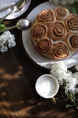 Cinnamon rolls on the table with white lilacs. Breakfast with rolls and milk.