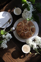 Cinnamon rolls on the table with white lilacs. Breakfast with rolls and milk.
