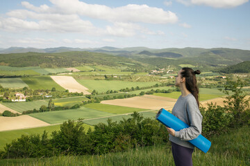 Woman with rolled fitness mat in her hands in the mountains