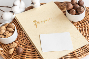 Naklejka na ściany i meble Stylish composition of blank business card photobook and delicious nuts lying on wicker tray on table extreme close view