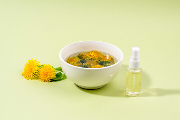 Dandelions (Taraxacum) in a bowl with boiling water and spray bottle with face toner. Home made beauty product.
